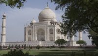 a white building with a dome and a lawn with Taj Mahal in the background
