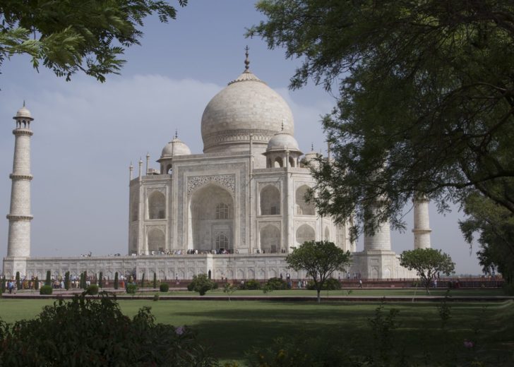 a white building with a dome and a lawn with Taj Mahal in the background