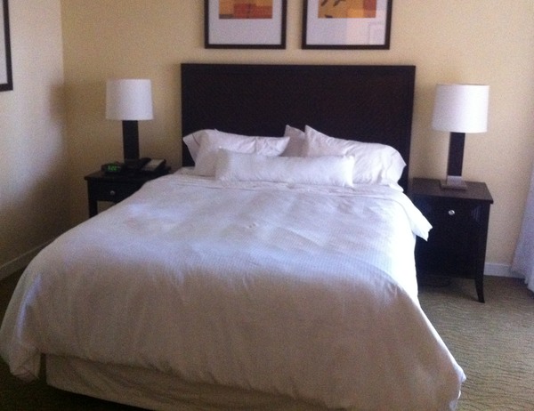 a bed with white sheets and lamps