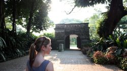 a woman standing on a path with trees and plants