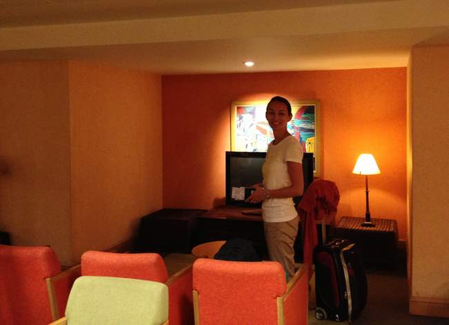 a woman standing in a room with chairs and a suitcase
