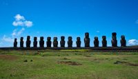 a row of statues in a field with Easter Island in the background