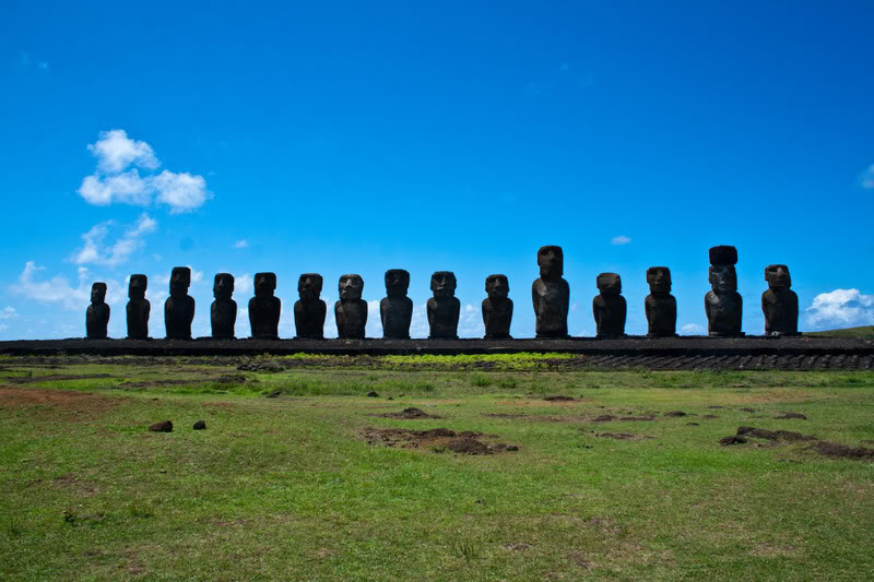 a row of statues in a field with Easter Island in the background