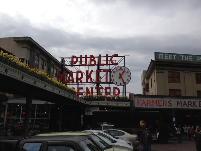 a sign with a clock on it with Pike Place Market in the background