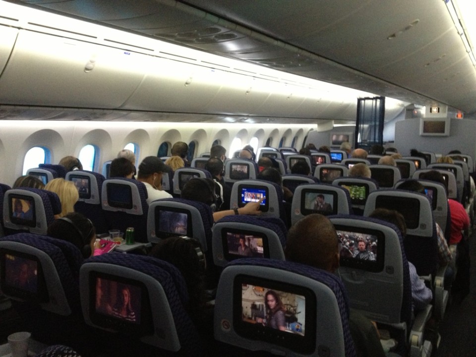a group of people sitting in an airplane with a television screen