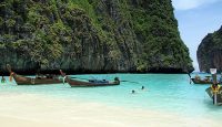 boats in the water near a cliff with Phi Phi Islands in the background