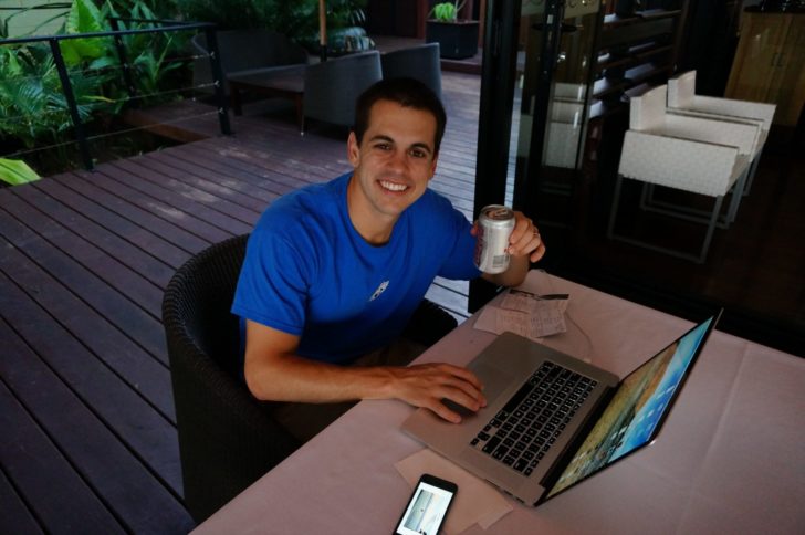 a man sitting at a table with a laptop and a can