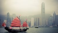 a boat with red sails in the water with a city in the background