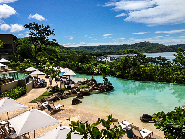 a pool with chairs and umbrellas and a body of water