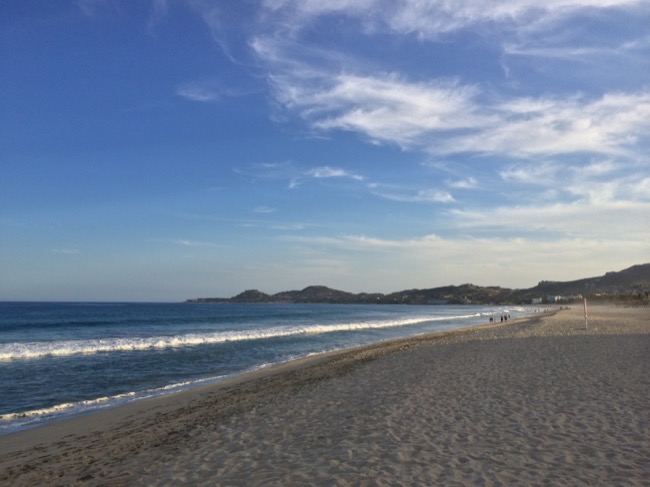 a beach with waves and hills in the background