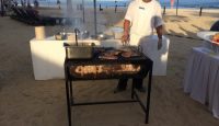 a man cooking meat on a grill on a beach