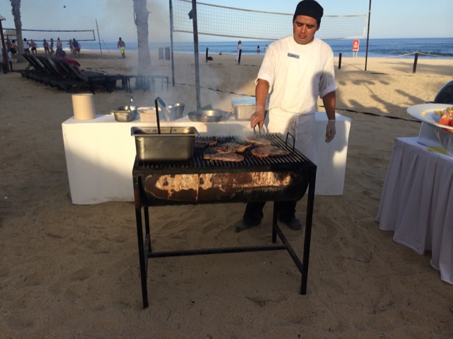 a man cooking meat on a grill on a beach
