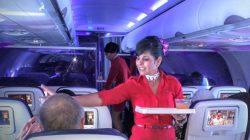 a woman in a red dress holding a tray in an airplane