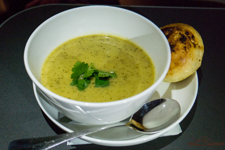 a bowl of soup with a spoon and bread on a plate