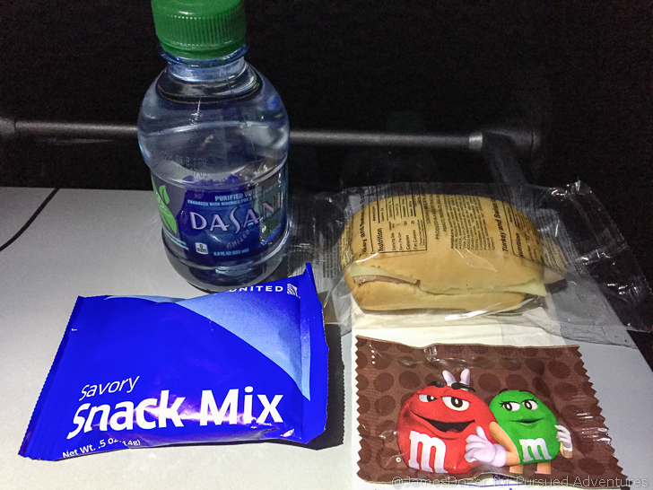 a sandwich and a bottle of water next to a snack mix