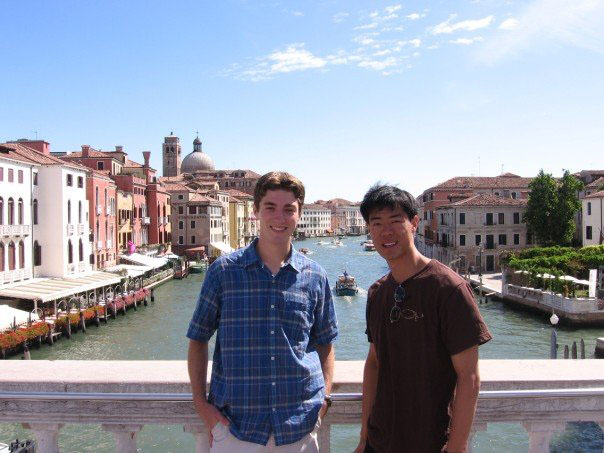 two men standing on a bridge over a river with buildings in the background