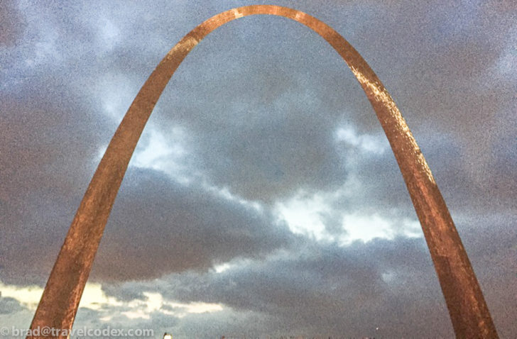 a large arch with clouds in the background