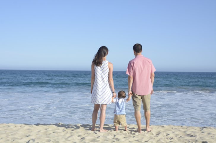 a man and woman holding hands with a child on a beach