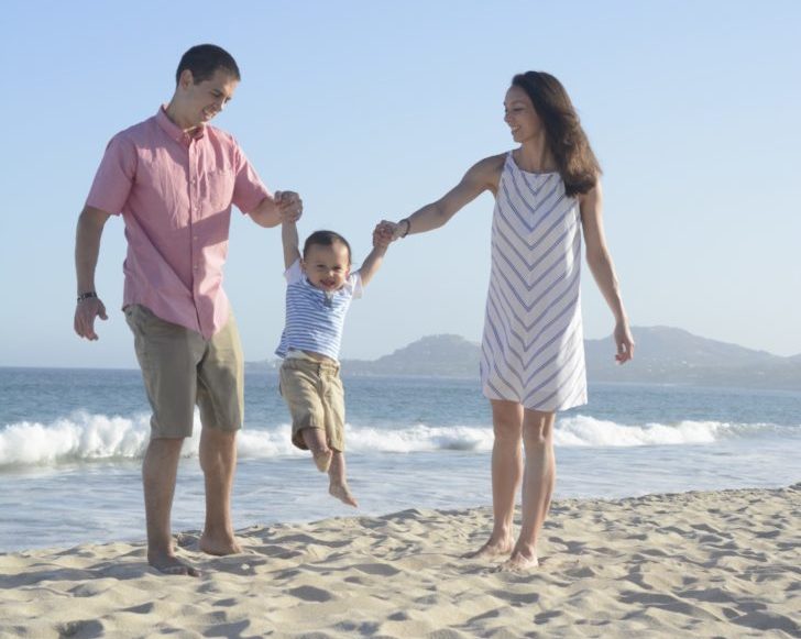 a man and woman holding a baby on a beach