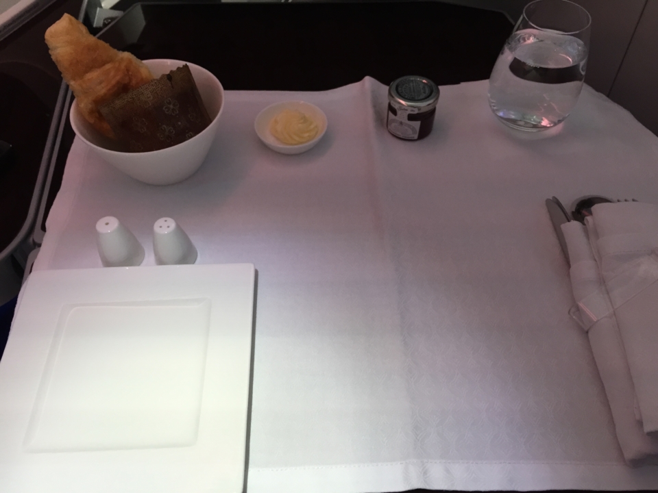 a table with a white cloth napkin and a bowl of bread and a glass of water