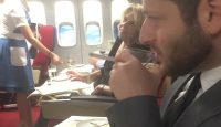 a man in a suit drinking from a glass on an airplane