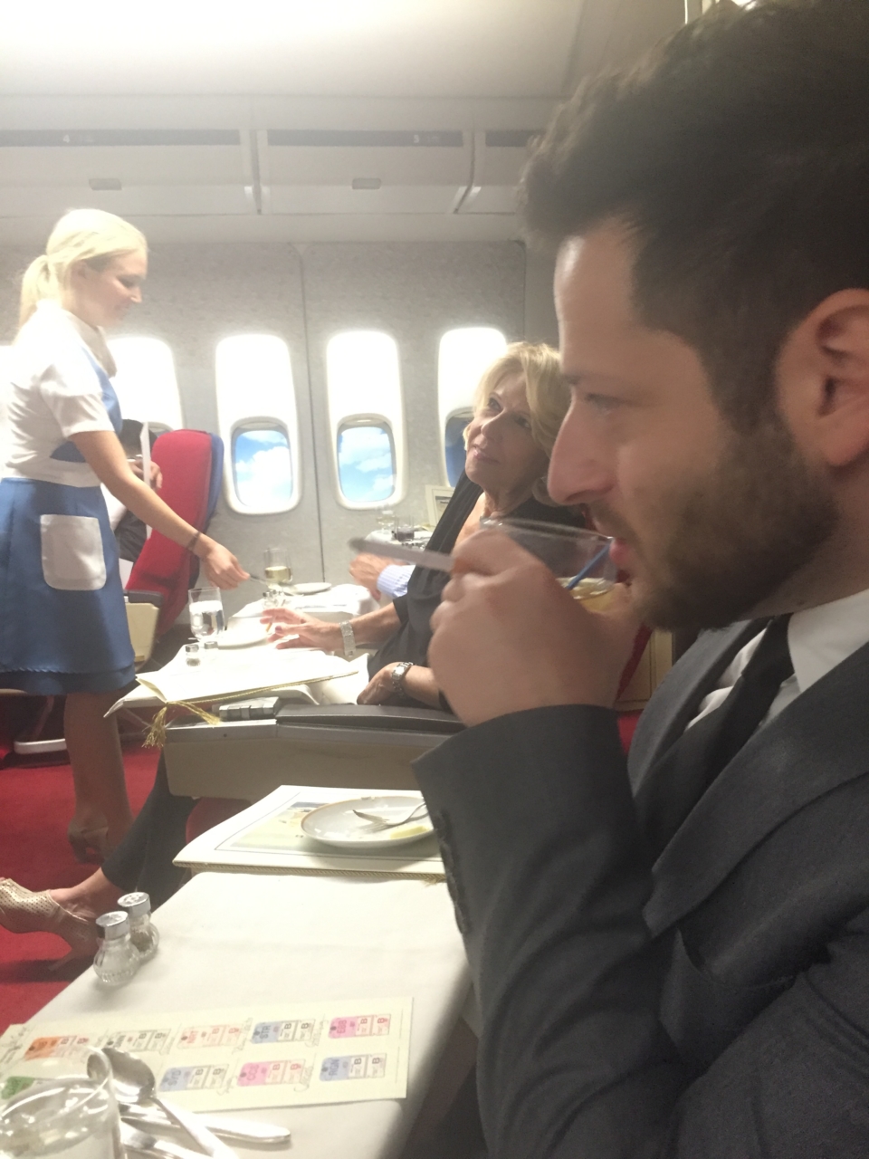 a man in a suit drinking from a glass on an airplane