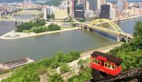 a train on a track with Duquesne Incline in the background