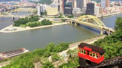a train on a track with Duquesne Incline in the background