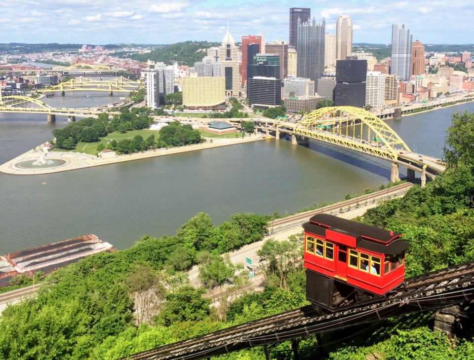 a train on a track with Duquesne Incline in the background