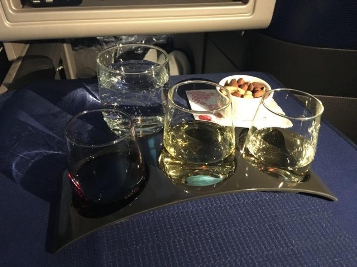 a tray of glasses with liquid and a bowl of nuts on a seat