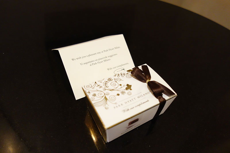 a small white box with a brown ribbon and a bow on a black surface