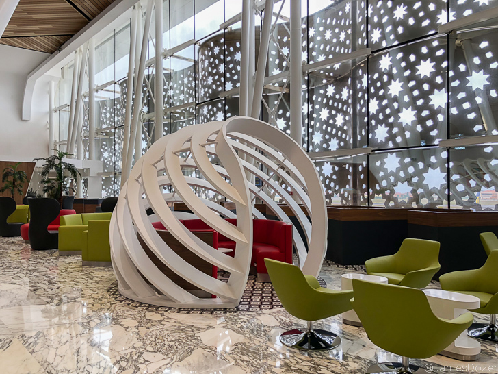 a white sculpture in a room with green chairs and a red chair
