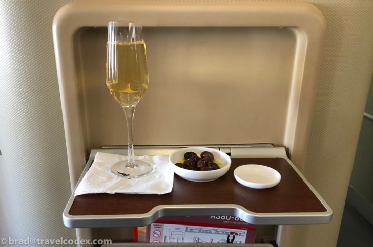 a glass of champagne and a bowl of olives on a tray