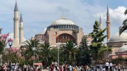 a group of people walking in a park with a large building with Hagia Sophia in the background