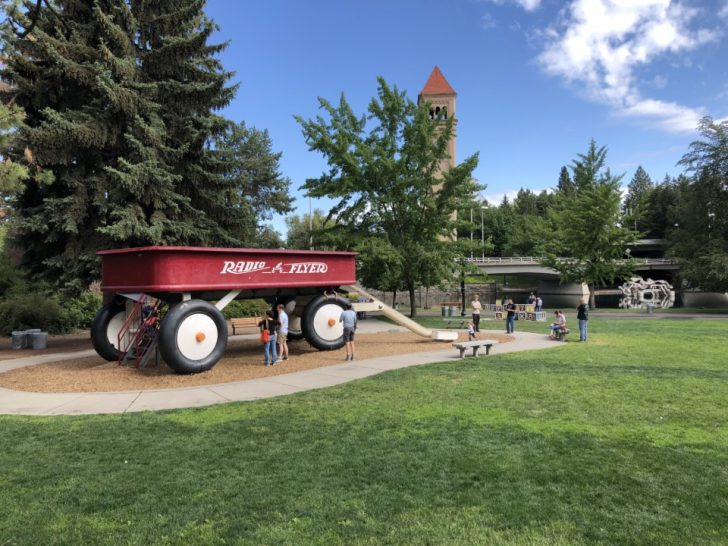 a red wagon with large wheels and people in a park
