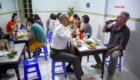 a group of people sitting at a table eating food and drinking