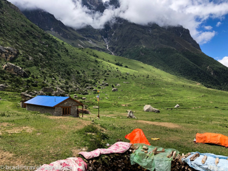 a stone building in a grassy field with mountains in the background
