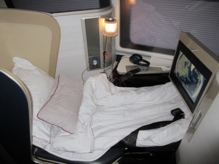 a bed with a white blanket and a tv on the back of a bed