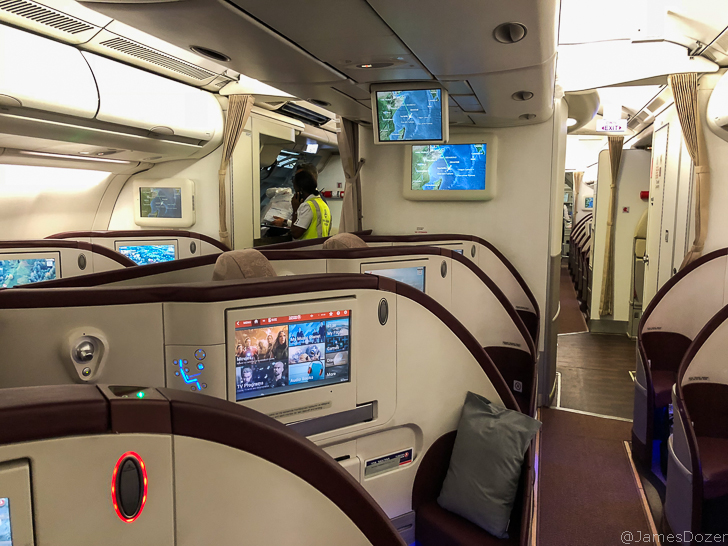 a interior of an airplane with monitors and a person standing in the background