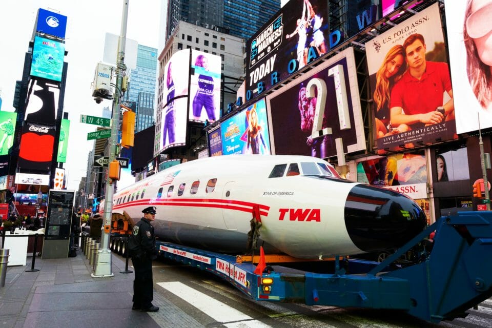 a man standing next to a white airplane on a flatbed trailer