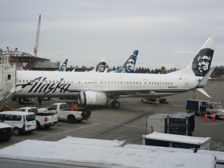 a large white airplane with blue tail fin and white truck parked in a terminal