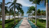 a walkway with palm trees and water with Laie Hawaii Temple in the background