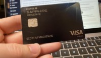 a hand holding a credit card in front of a laptop