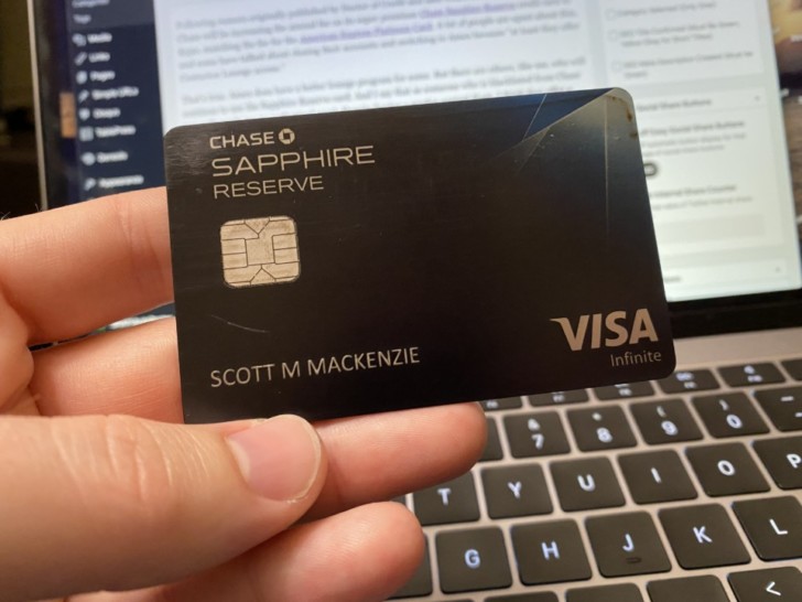 a hand holding a credit card in front of a laptop