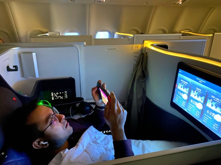a man sitting in an airplane with a phone and a monitor