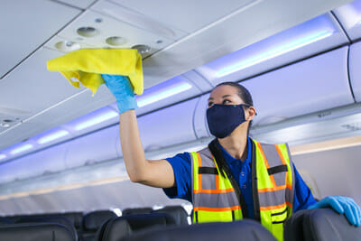 a woman wearing a mask and gloves cleaning an airplane
