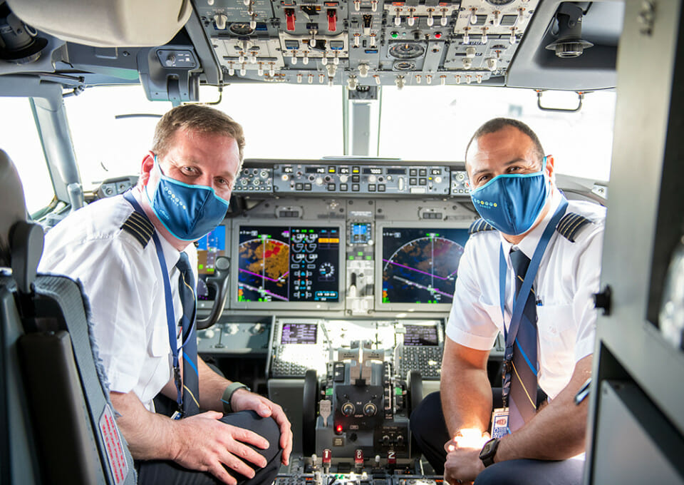 two men wearing face masks in a cockpit of an airplane