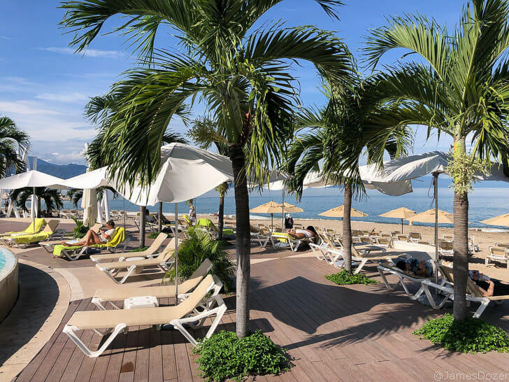 a group of people sitting on lounge chairs and umbrellas on a beach