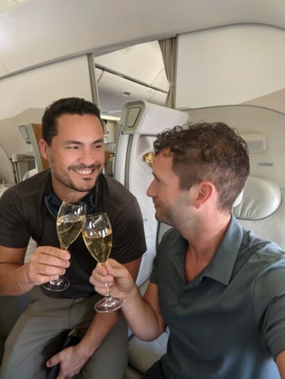 two men sitting in an airplane holding wine glasses