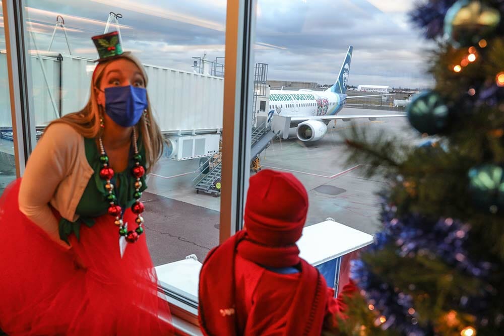 a woman wearing a mask and a hat looking out a window at an airplane